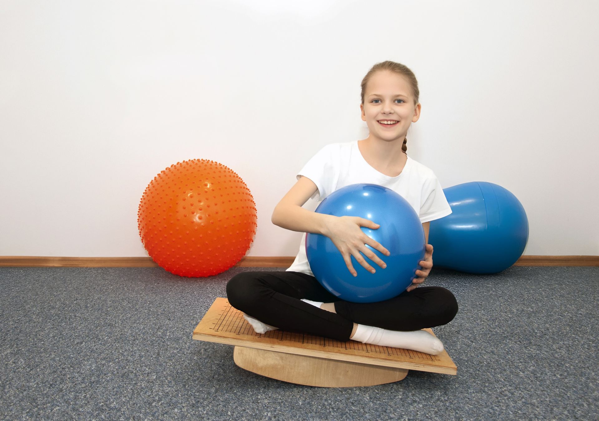 занятие по мозжечковой стимуляции в Центре развития Взлёт: девочка сидит на балансировочной доске занятие по мозжечковой стимуляции в Центре развития Взлёт: девочка сидит на балансировочной доске