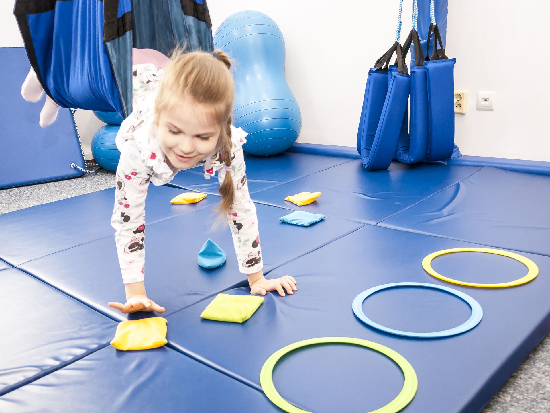 Dziewczynka wykonuje zadanie koordynacyjne na huśtawce sensorycznej w Centrum Wzlot w Krakowie Terapia sensoryczna – dziecko wzmacnia koordynację i koncentrację podczas dynamicznego ćwiczenia z workami i obręczami