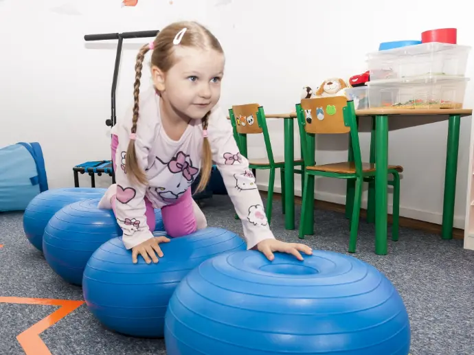 Zabawa z piłkami sensorycznymi rozwija równowagę, stabilność ciała i poczucie kontroli nad ruchem — ważne dla przygotowania do szkoły. Dziecko pokonuje tor przeszkód na piłkach sensorycznych w Centrum Wzlot w Krakowie
